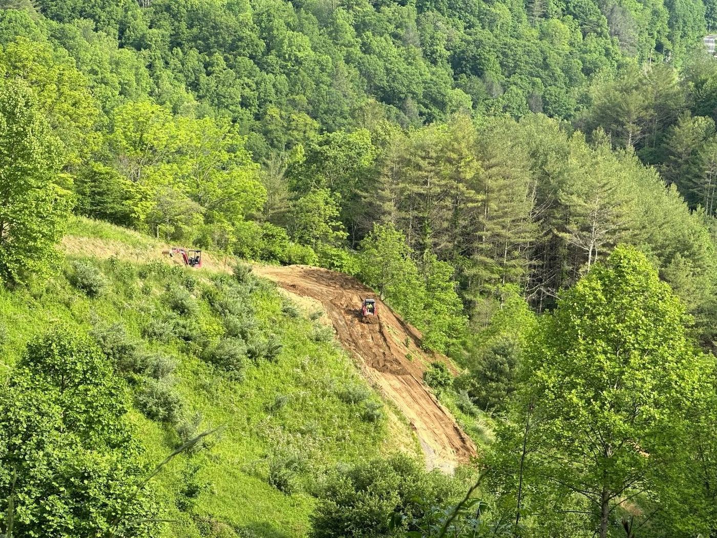 Dozer cutting a path across a steep green mountainside