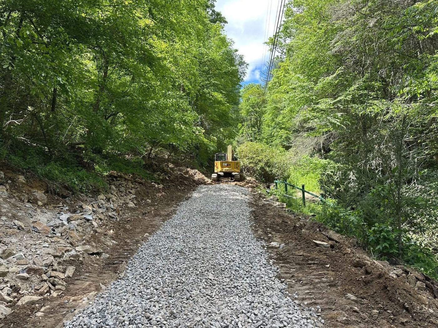 Fresh gravel access road through the woods with an excavator at the far end
